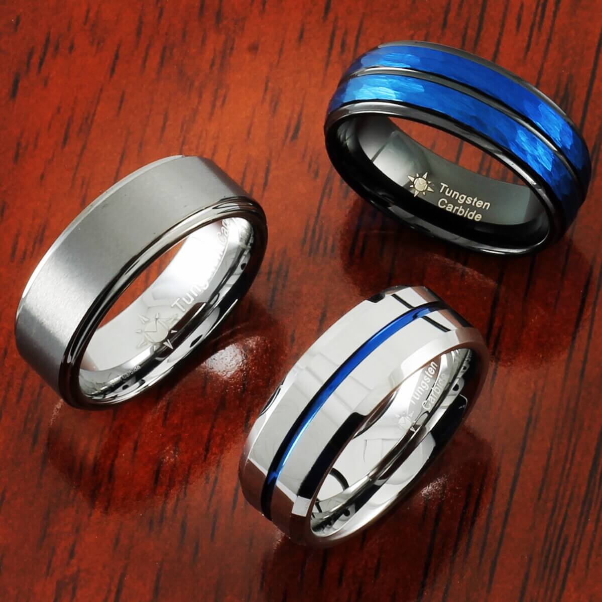 Gunmetal step ring, dual hammered blue inlay ring, silver beveled ring with then blue center inlay standing on wood 
