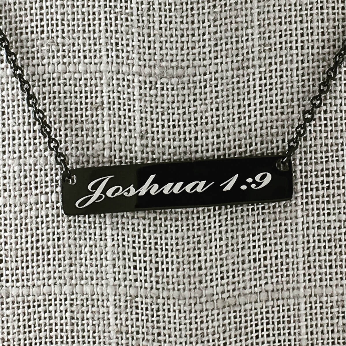 Bar pendant necklace with Joshua 1:9 engraved.  Textured cloth background